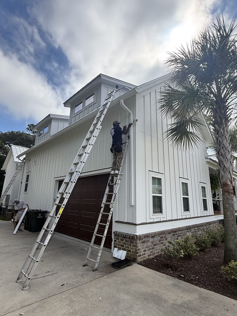 Installer on a ladder at a home framed by palmettos