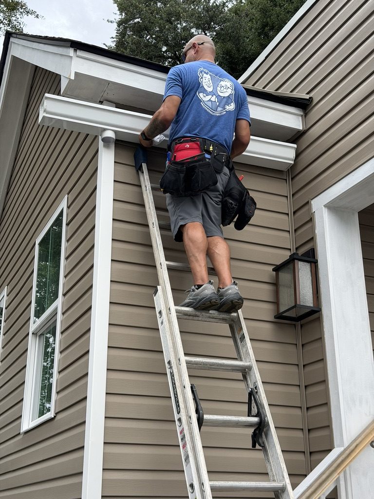 Installer on a ladder hanging a gutter on a two story home